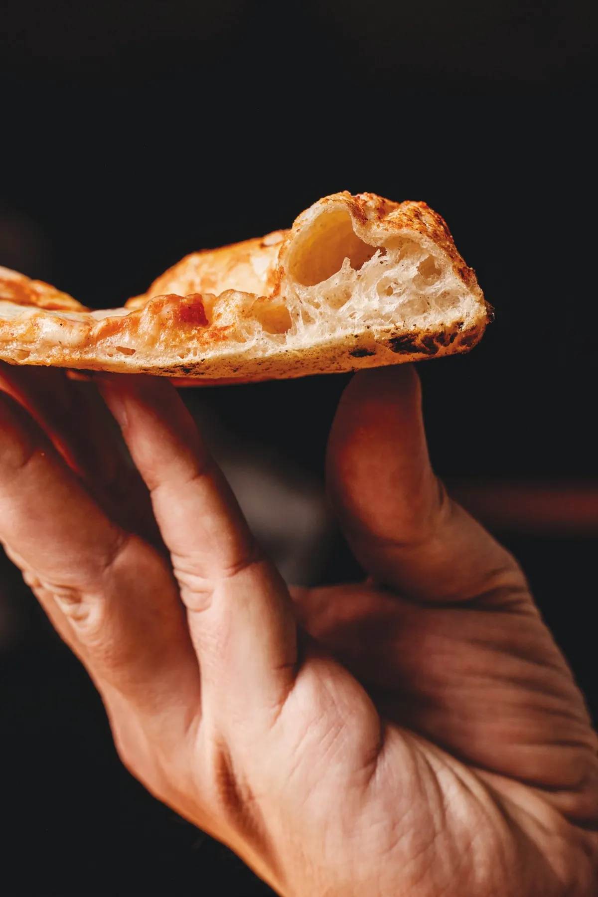 A hand holding a slice of Artisan pizza showing the airy crust